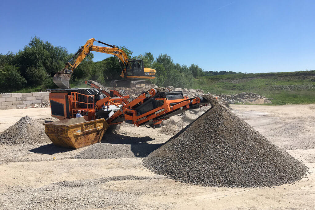 Mobile compact impact crusher recycling concrete at a recycling center with a blue sky in the background